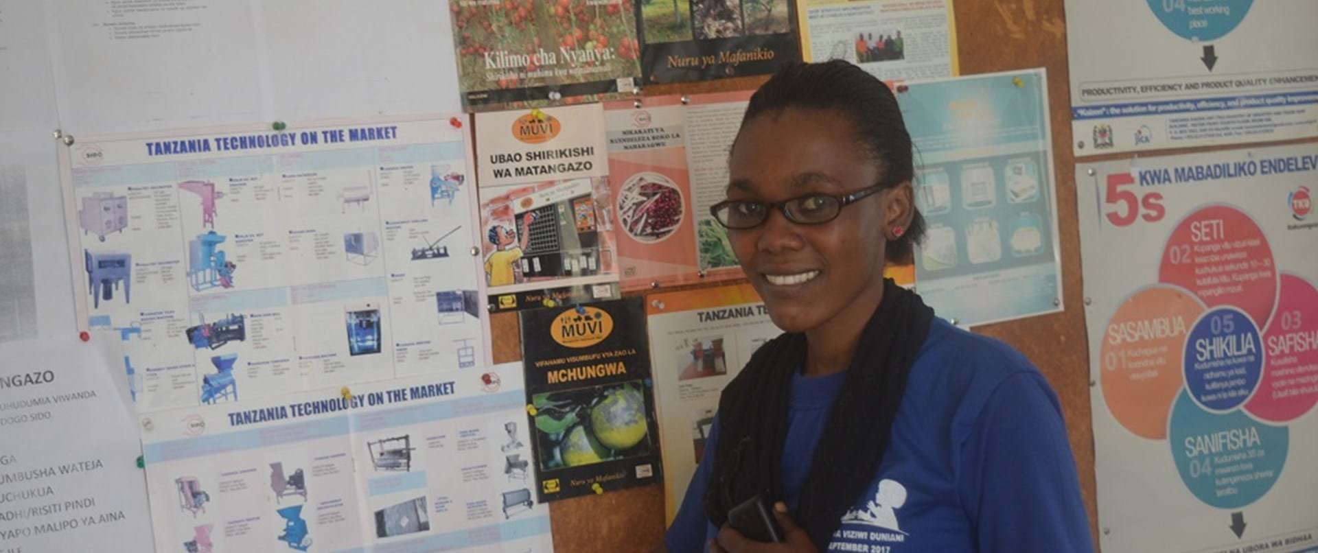 A young woman wearing glasses standing in front of a notice board