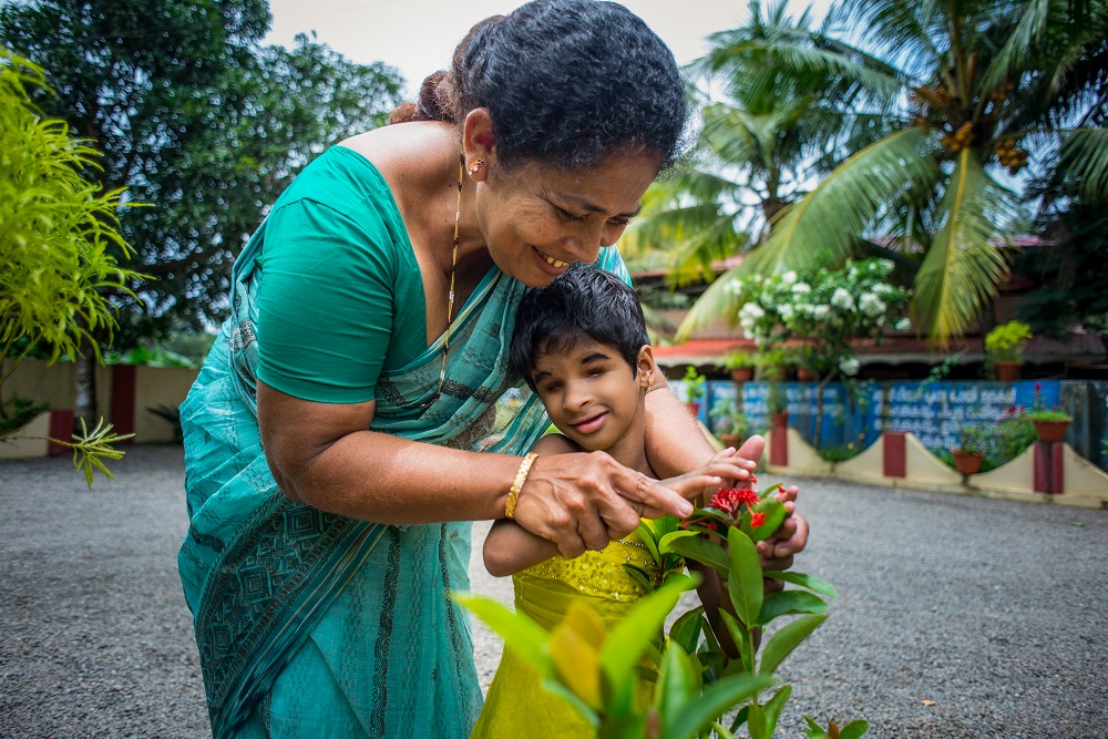 A woman helping a young girl touch plants in the garden