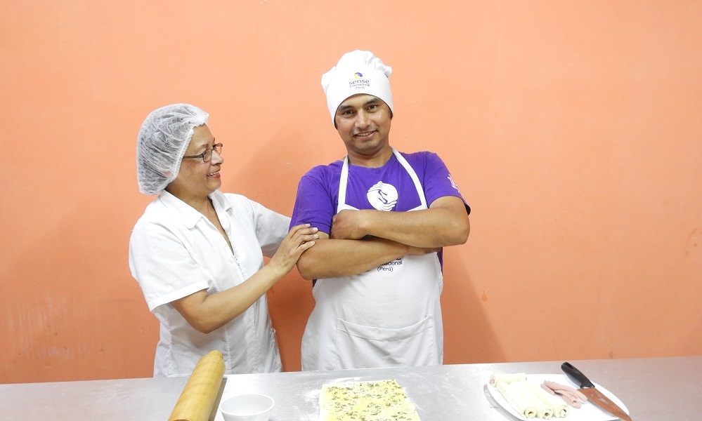 A woman standing next to a young man in a chef's hat. They are cooking.