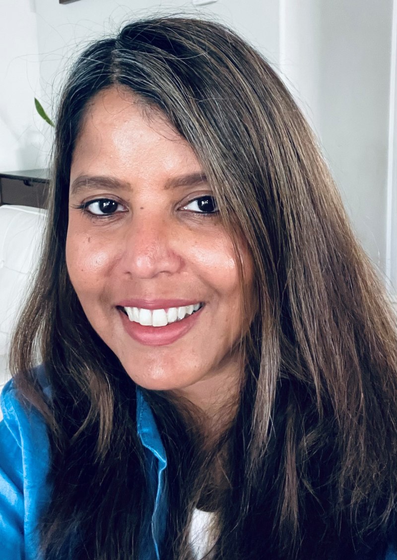 A woman with long hair and blue top smiling at the camera