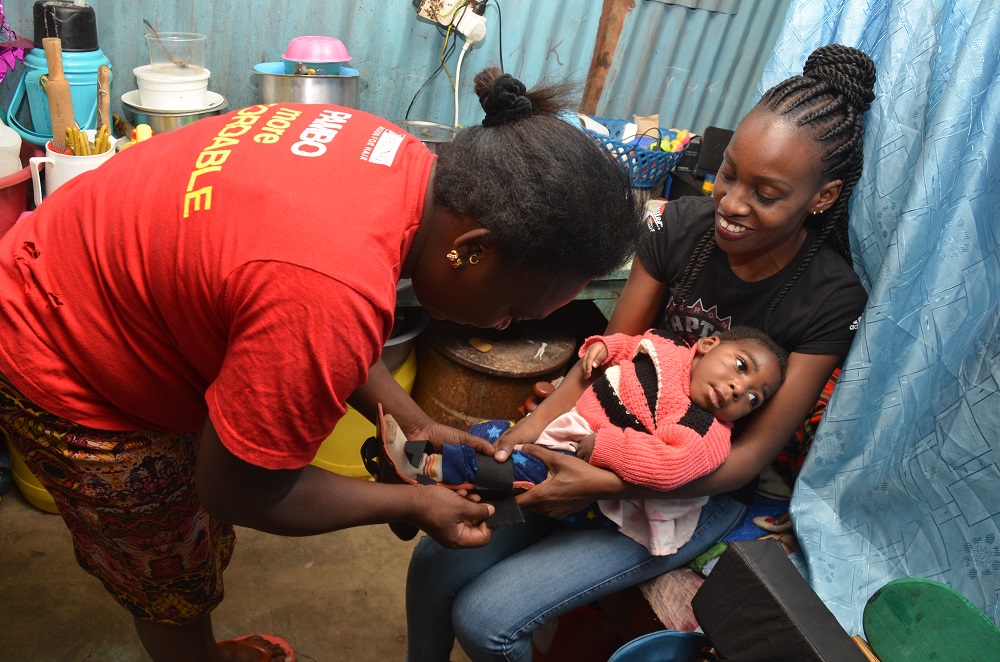 A doctor putting a brace on the leg of a baby who is sat on their mother's lap