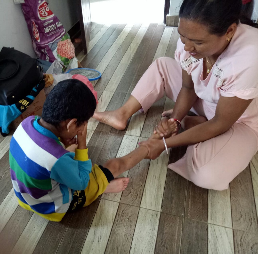 A boy sits on the floor whilst a woman rubs his feet