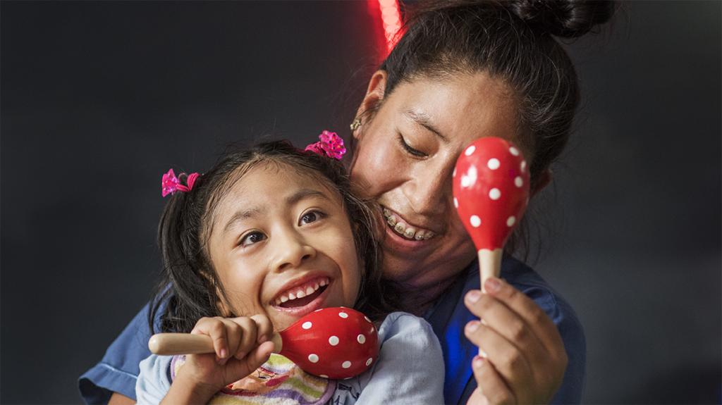 A young girl smiles as rattles are played 