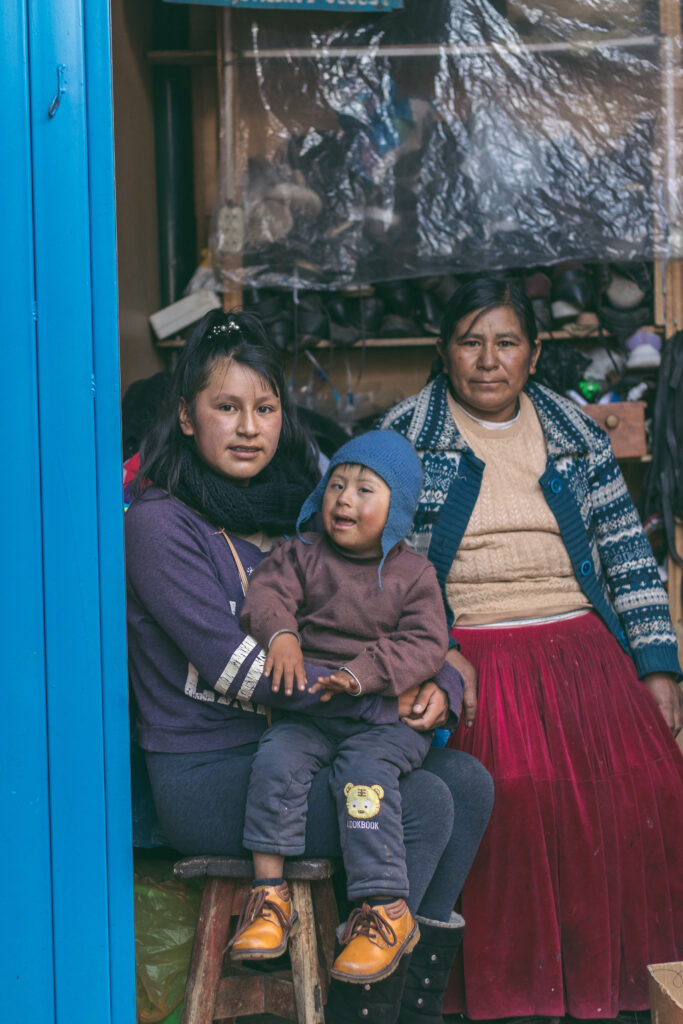 Angel, a young boy in a blue hat, is sat on his sisters lap. Their mother is sat behind them.