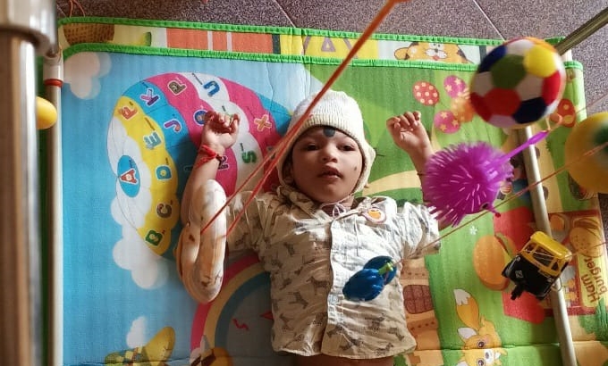 A child recieving visual therapy. He is lay on a mat and objects are being used to stimulate his vision.