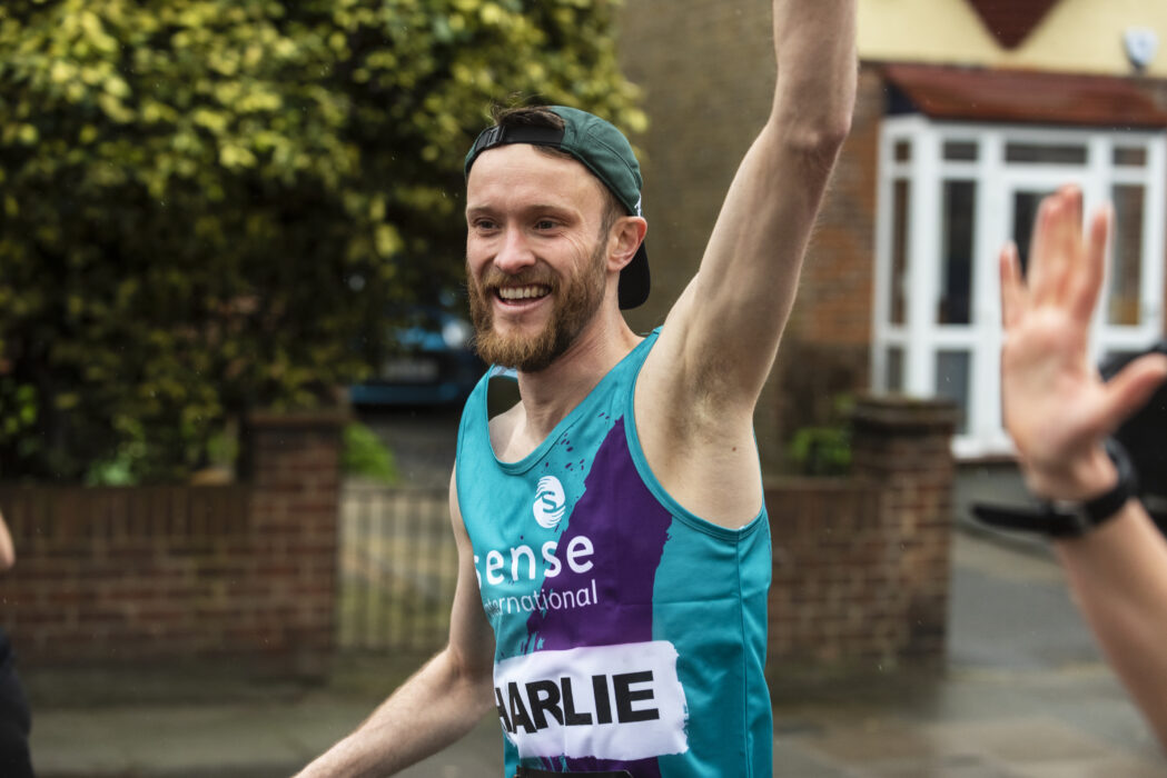 A marathon runner for Sense International waving at the camera.
