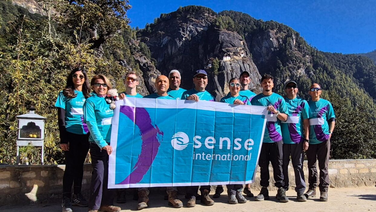 A group of people standing in front of a mountain range and holding a Sense International banner.
