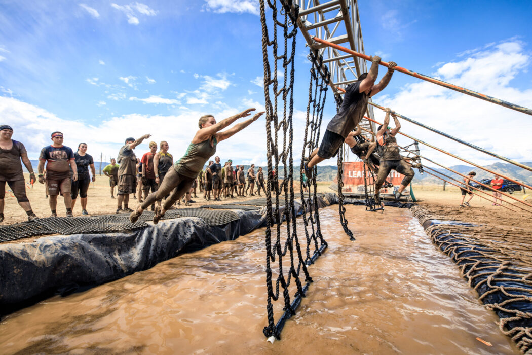 People swing across ropes over a pool of mud