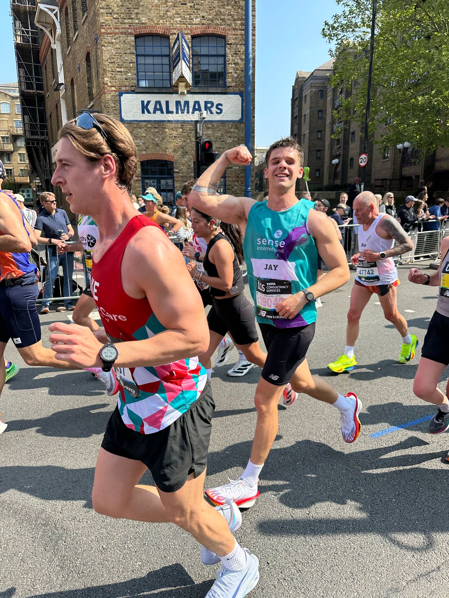 A young man wearing a Sense International running shirt flexes his bicep as he runs past