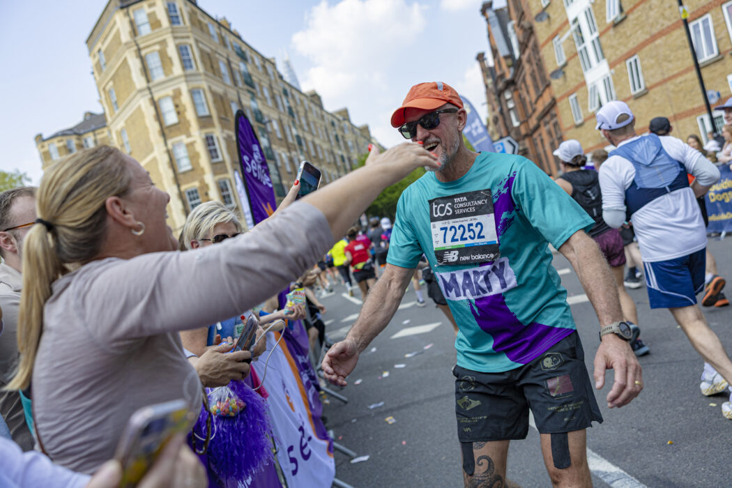 A man wearing a Sense International running vest spots his wife as he runs past