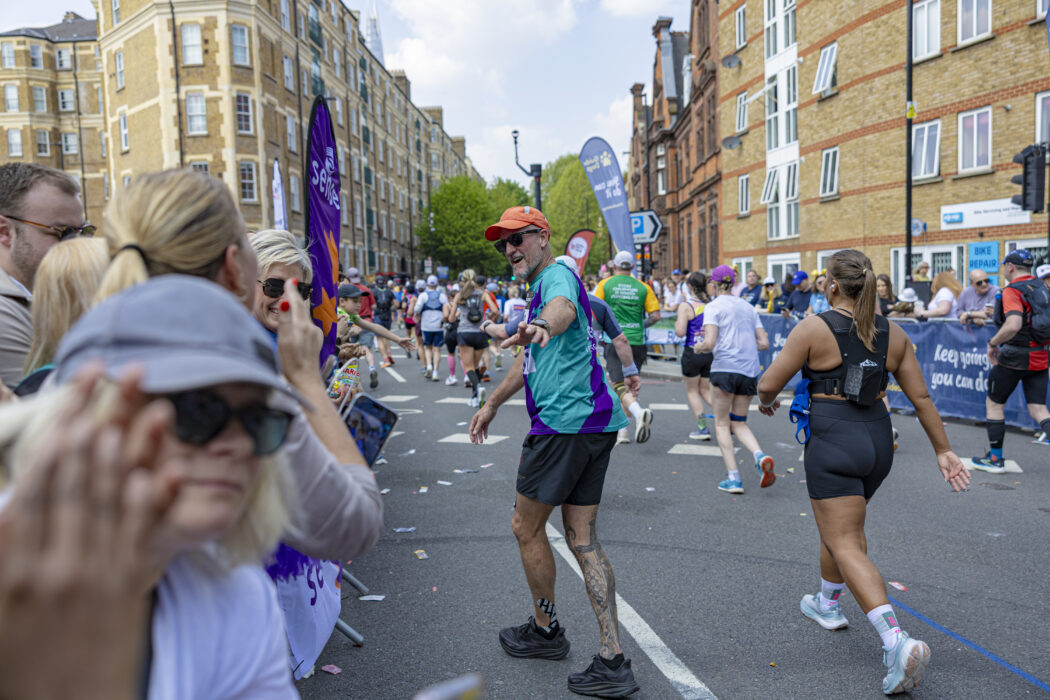 A man wearing a Sense International running vest waves as he runs past