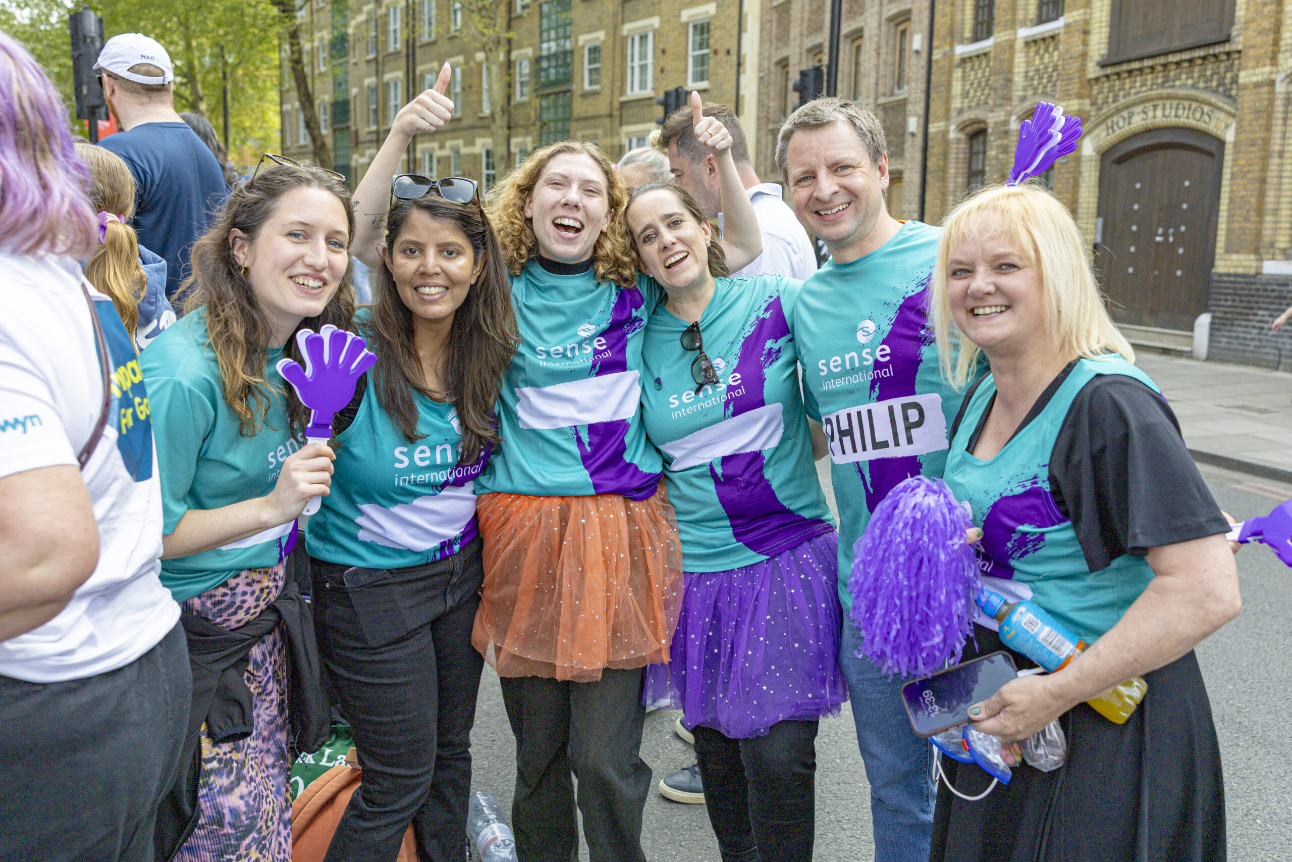 A group of supporters wearing Sense International t shirts cheer at the camera