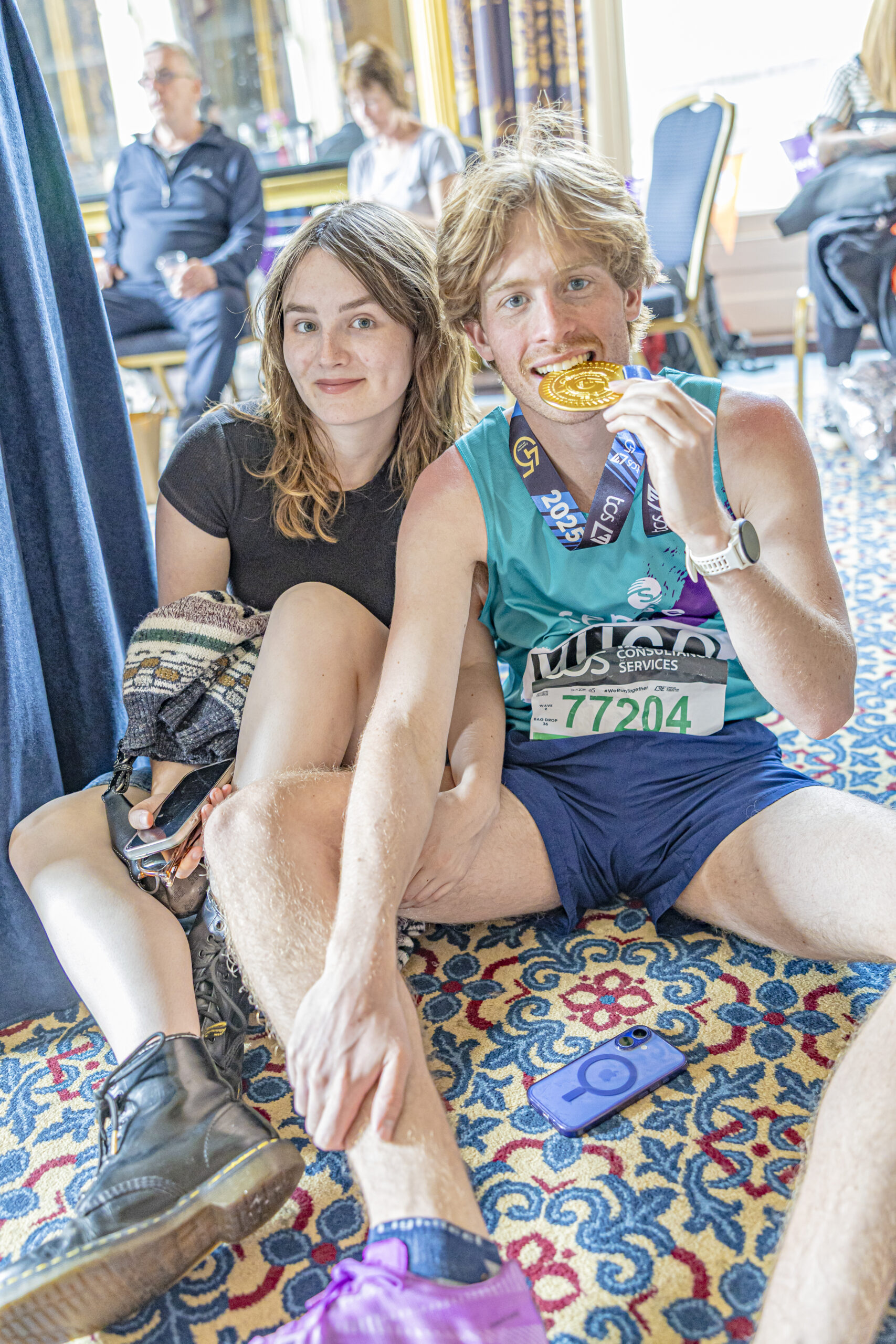 A young man wearing a Sense International running vest bites his London Marathon medal