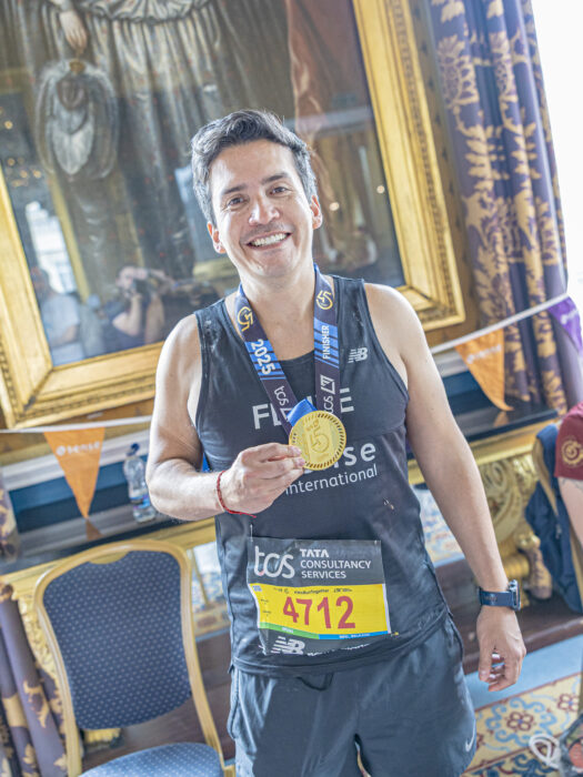 A man wearing a Sense International running vest holds his London Marathon medal