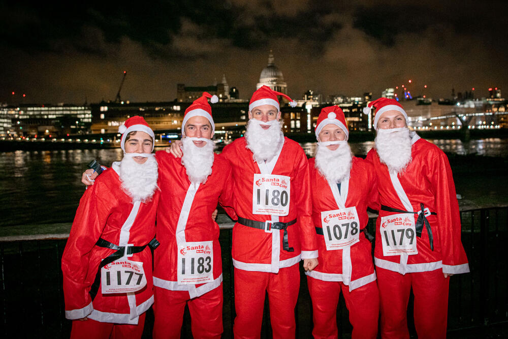 A group of people wearing Santa outfits and fake beards pose for a photo