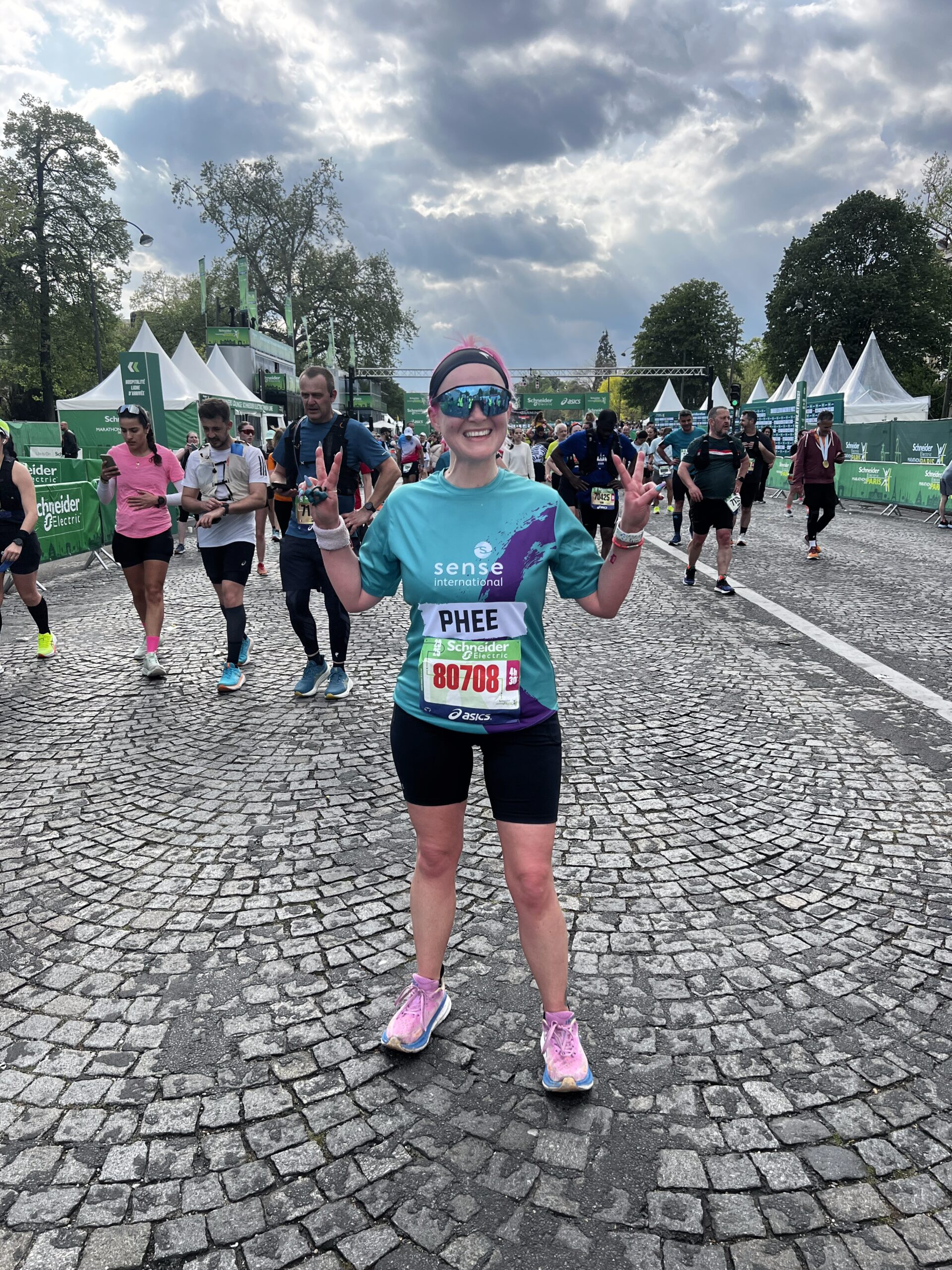 A woman wearing a Sense International running shirt throws a double peace sign