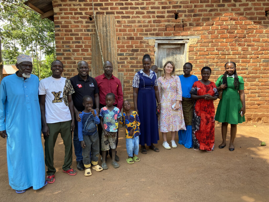 A large family of various ages and three young children stand in a line next to a Sense International representative.