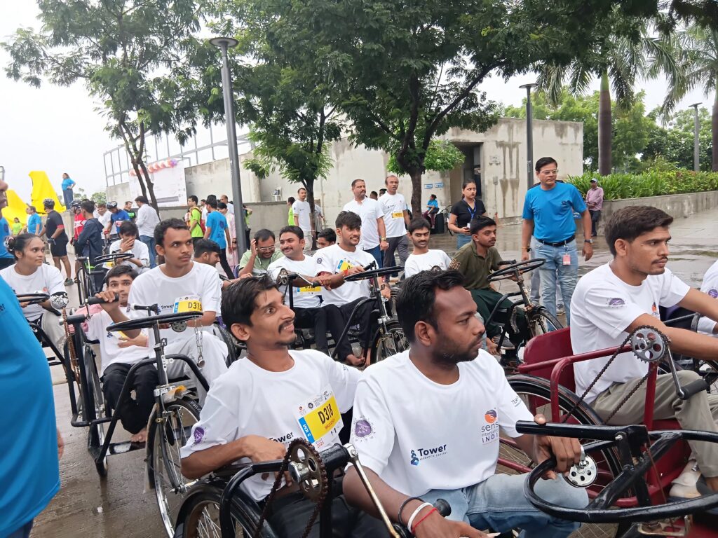A crowd of people wearing white t shirts with the Sense International Logo ride on tricycles
