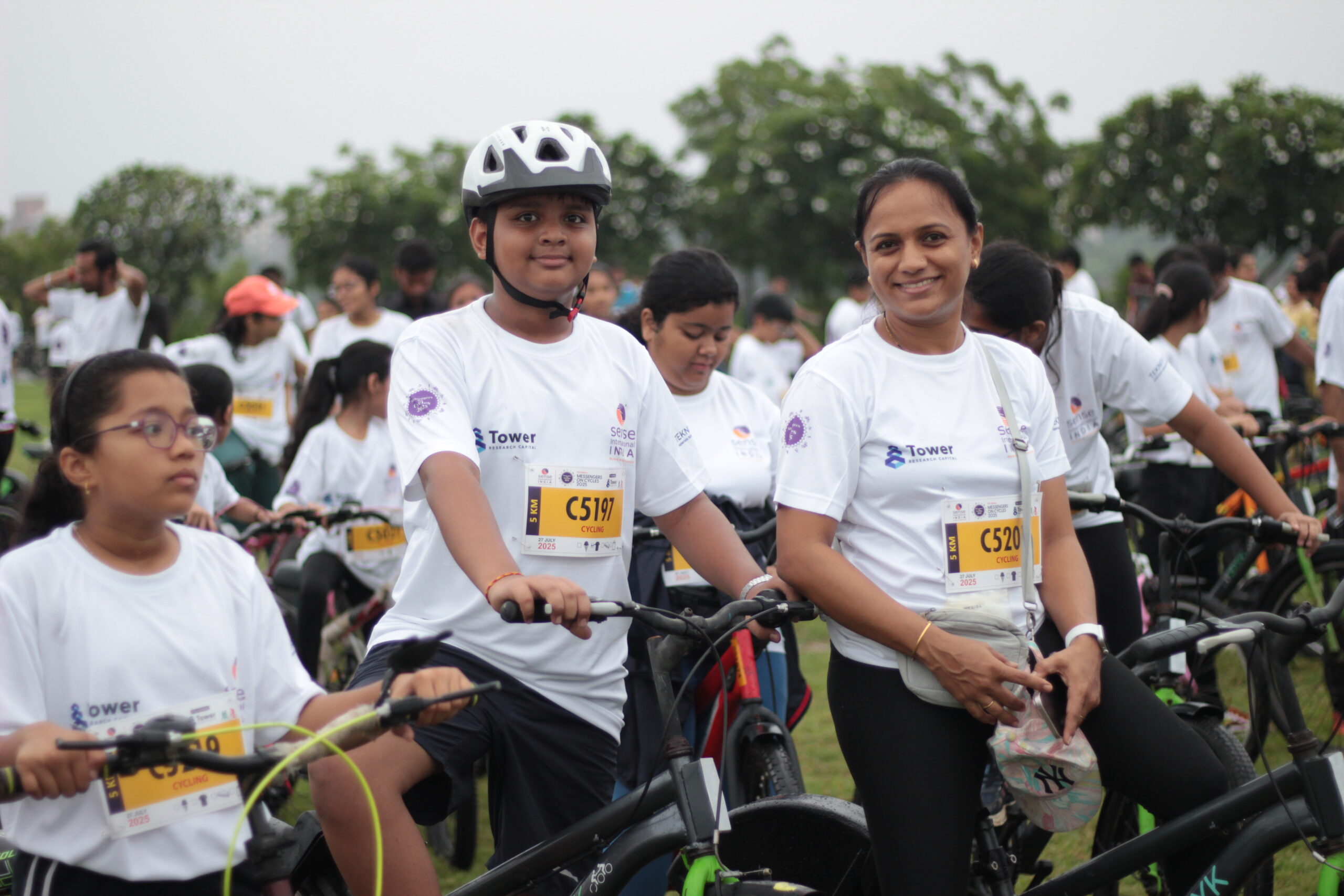 A large crowd of people wearing white shirts featuring the Sense International India logo stand with bicycles