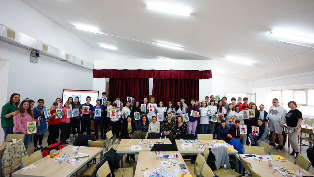 A huge crowd of teachers and teenage students stand in line in a classroom. They are holding up colourful sensory paintings they have created,
