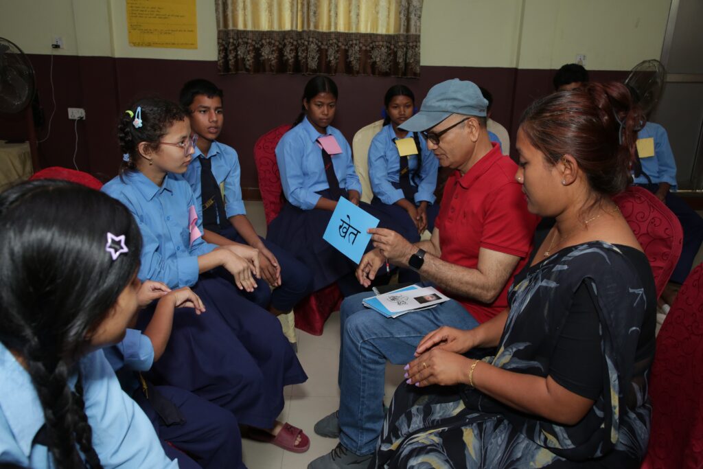 Six Nepali students wearing blue school uniforms and ties learn from their educators using language cards.