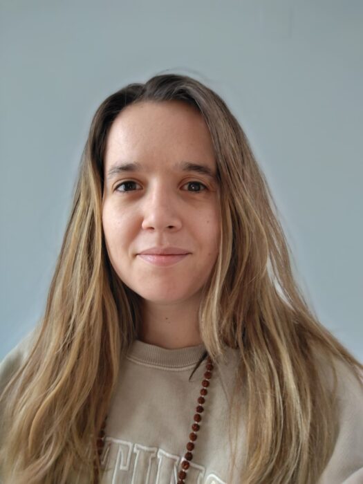 A young adult white woman with long blonde hair smiles at the camera