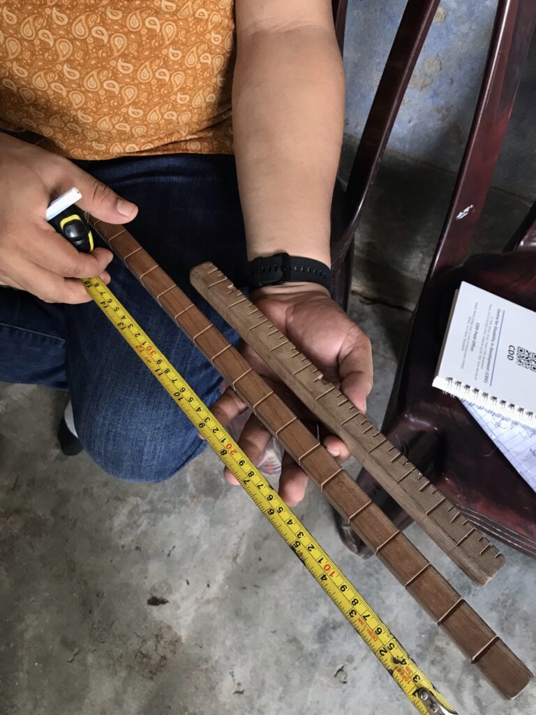 A pair of hands holding one standard measurement tool alongside two tactile measurement tools with deep grooves for blind workers to feel measurements