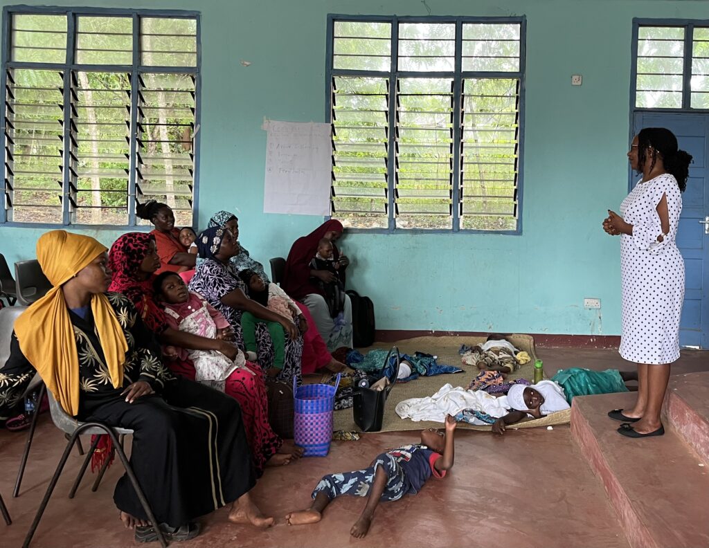 In a turquoise green room a group of Kenyan mothers wearing colourful clothing with several children laying on the floor
