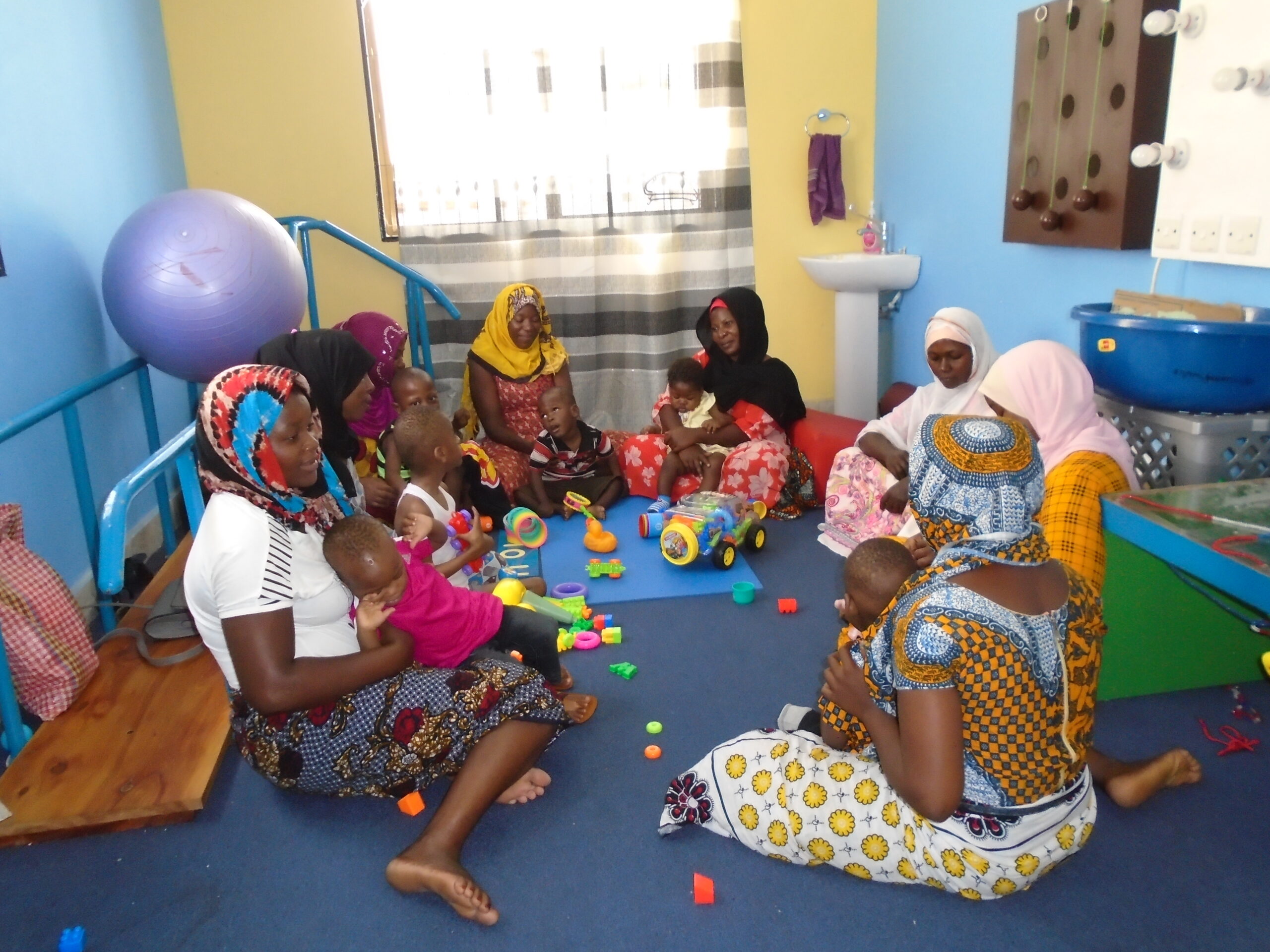 In a bright blue playroom full of colourful toys, parents engage with their young babies