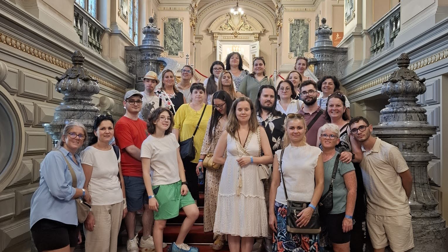 A large group of around 30 Romanian young adults in colourful clothing standing on the stairs of a museum.