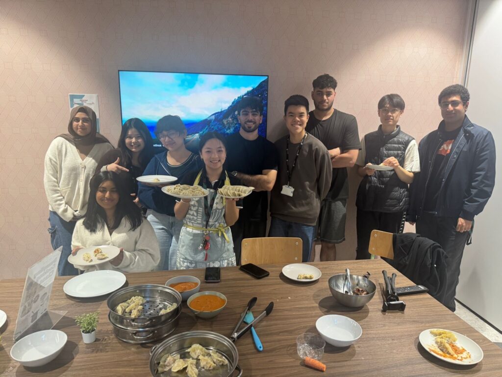 A group of students holding plates and bowls of dumplings as they smile at the camera