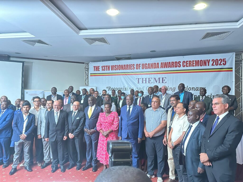 A large crowd of Ugandan adults pose in front of a banner which reads 'The 13th Visionaries of Uganda Awards Ceremony 2025'