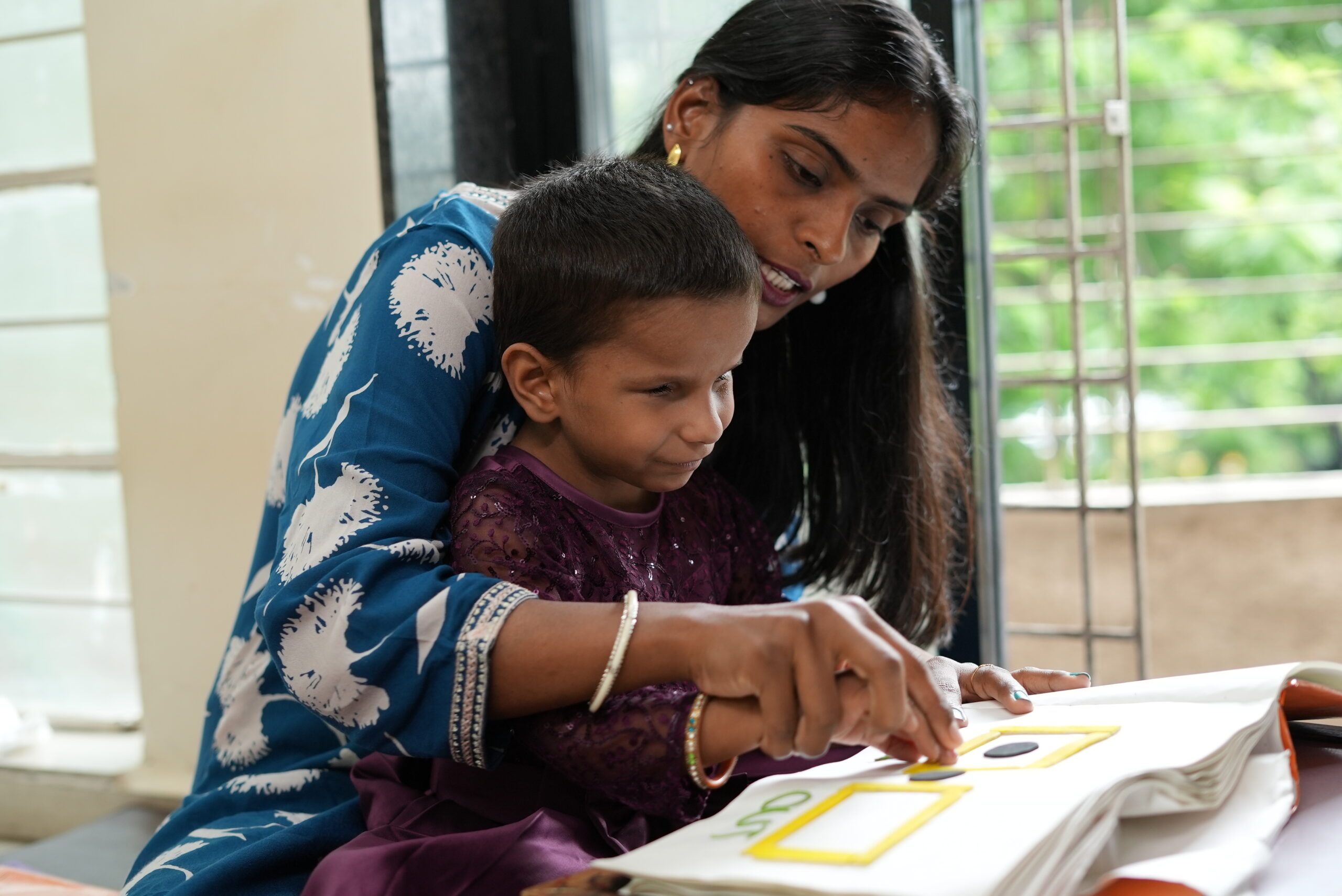 A young Indian girl with facial deformities is guided to read braille by a special educator