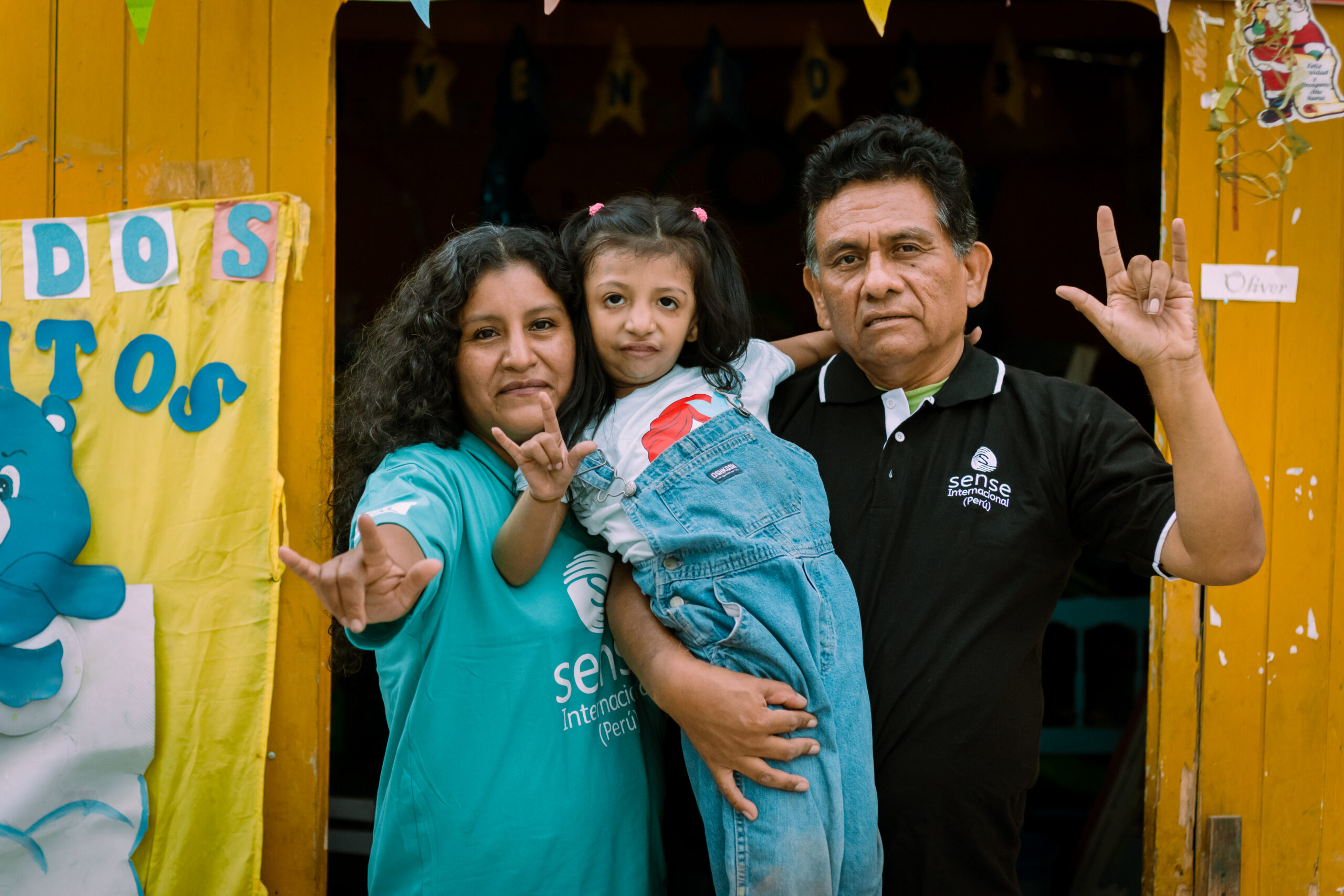 A Peruvian family including a mother and father holding a little girl with Down's Syndrome, all making the sign for 'I love you'