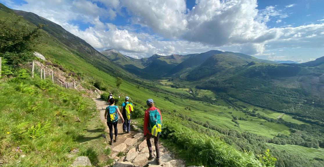 A group of hikers in colourful gear trek the stunning green landscape of Ben Nevis.