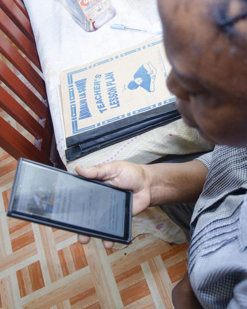 An adult Tanzanian woman looks at a phone screen which shows the homepage of the Global Deafblindness Resource Hub