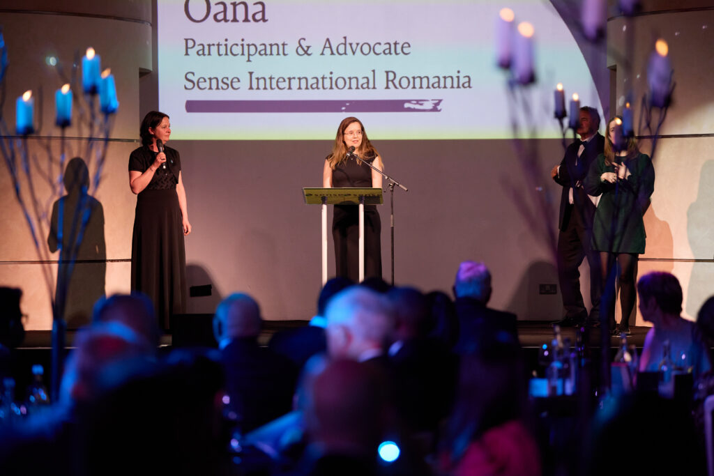 Oana, a participant and deafblindness activist from Romania, speaks at a lectern at the Sense International Changemakers Gala