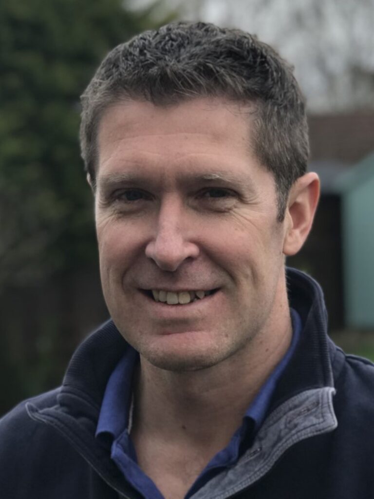 Headshot of a white man with dark grey hearing a fleece