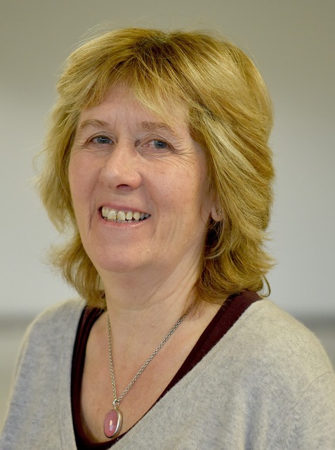 Headshot of a white woman with short layered blonde hair wearing a grey top