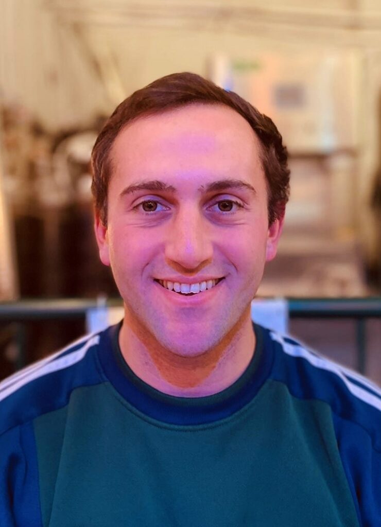 Headshot of a young white man with dark hair wearing a green sweatshirt