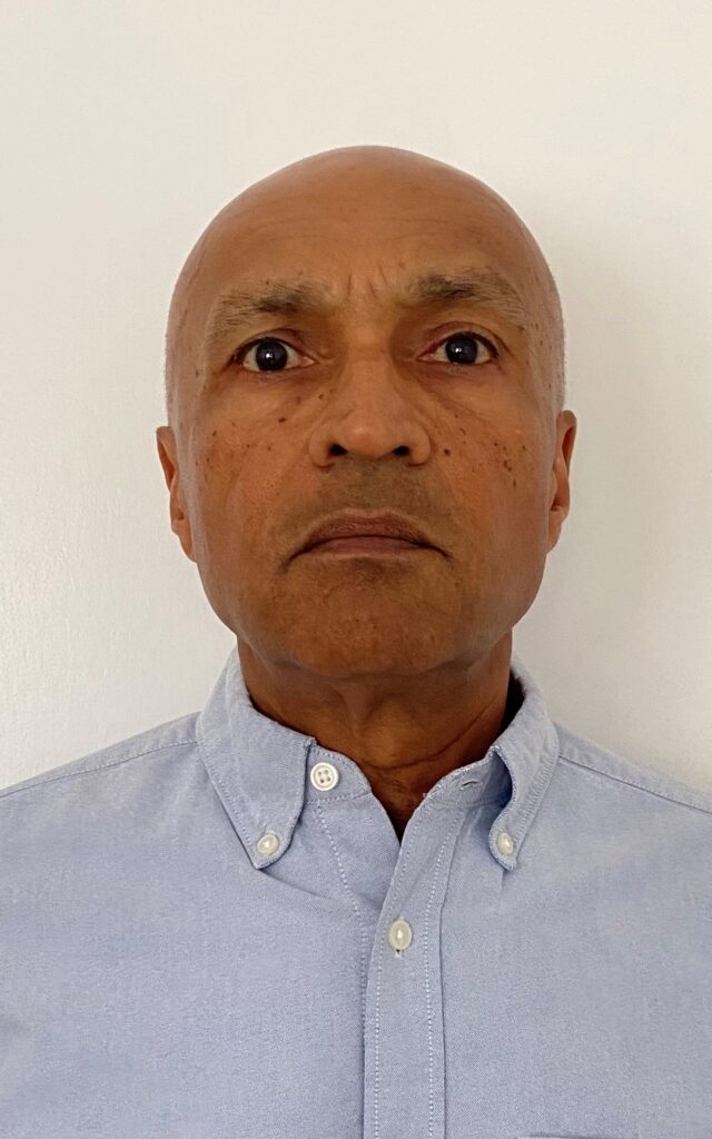 Headshot of bald South Asian gentleman wearing a blue shirt