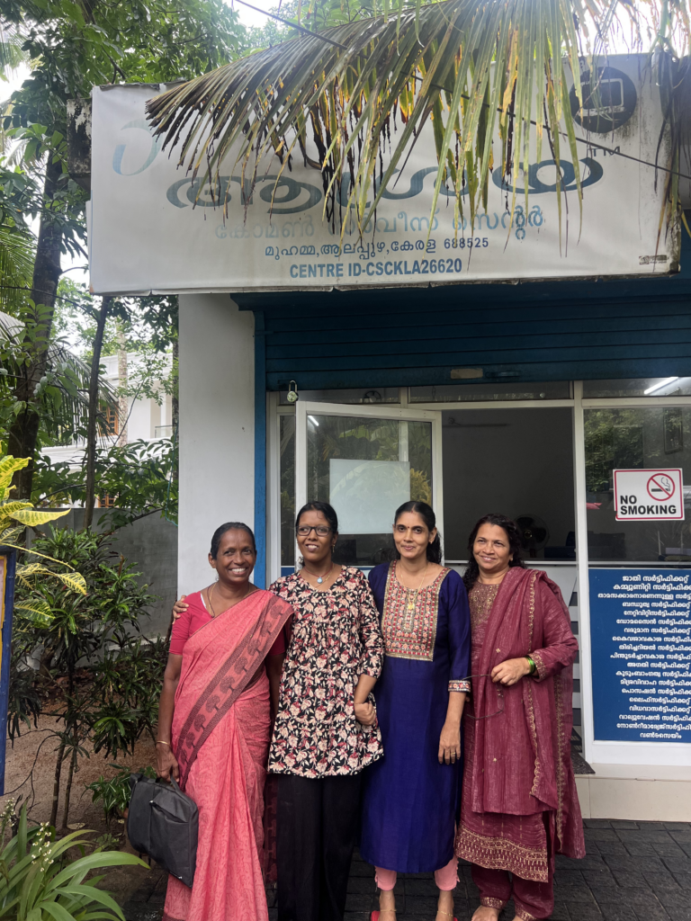 Three Indian women wearing saris stand in front of a government centre