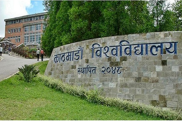 A brick wall with Nepali text reading 'Kathmandu University'